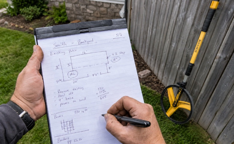A contractor sketching site measurements onto a notepad beside a measuring wheel